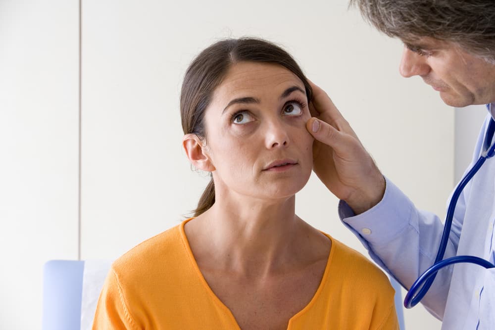 A doctor screens a female patient for anemia by examining her eyes
